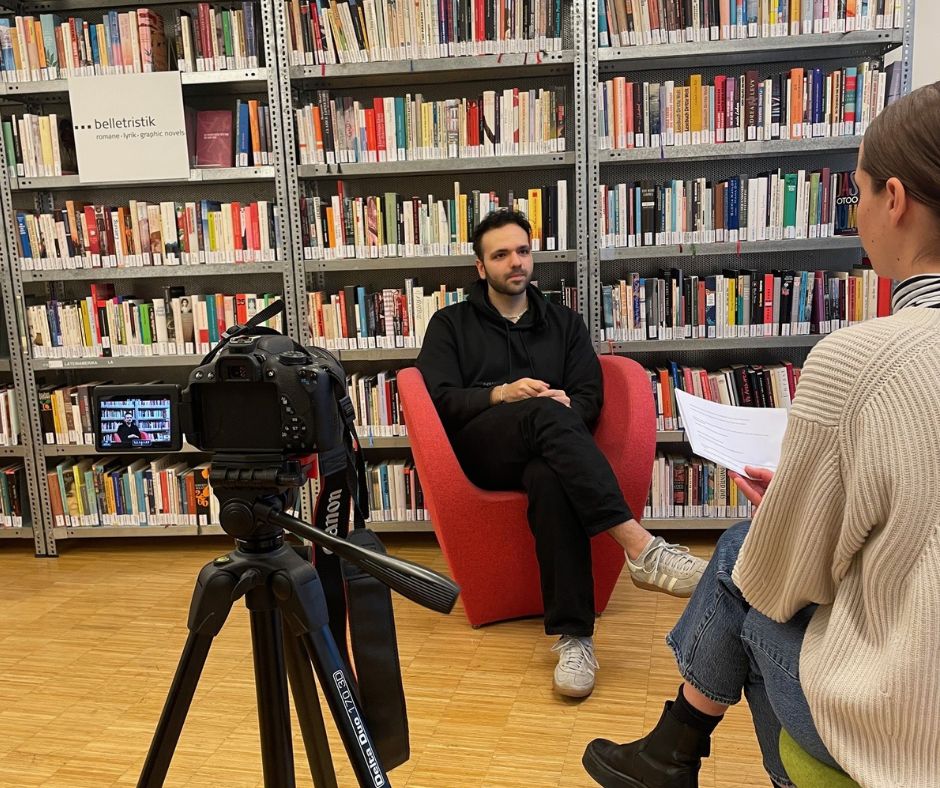 Der C3-Award Preisträger sitzt vor einem Bücherregal und wird interviewt. Außerdem kann man eine Kamera sehen, die das Interview filmt.